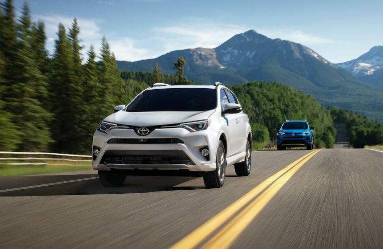 A front view of two versions of the 2018 Toyota RAV4 driving on a road.