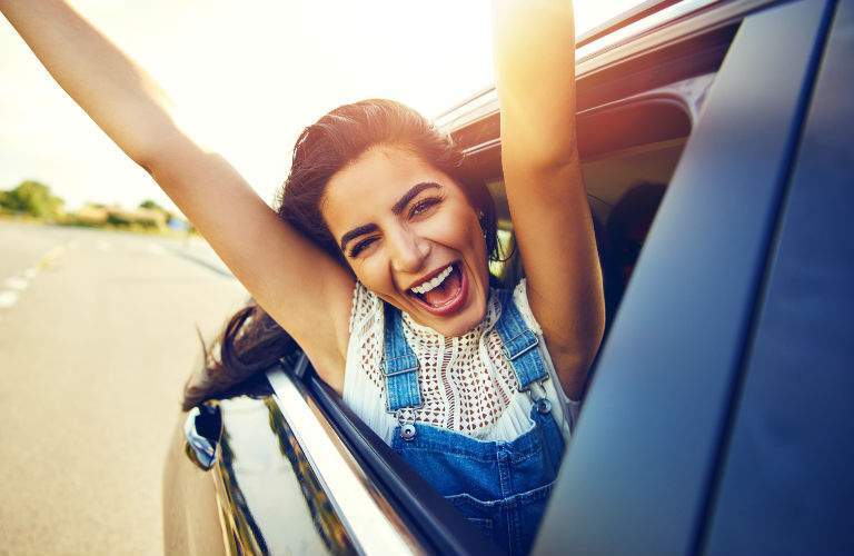 Excited Woman Extending Arms out of Passenger Window of New Car with Smile on Her Face
