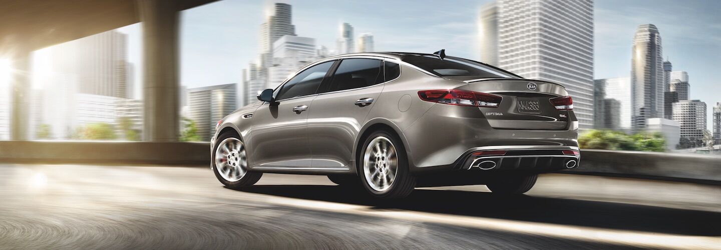A gold Kia Optima driving through a city A gold Kia Optima driving under a bridge in the city