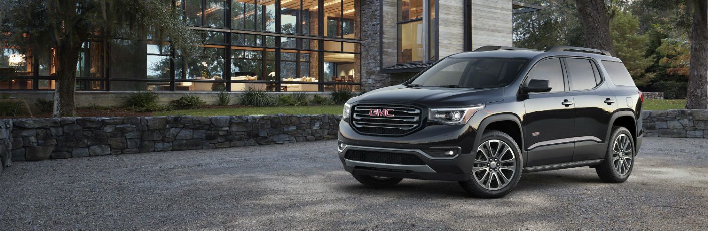 A left profile photo of the 2019 GMC Acadia parked in front of a house.