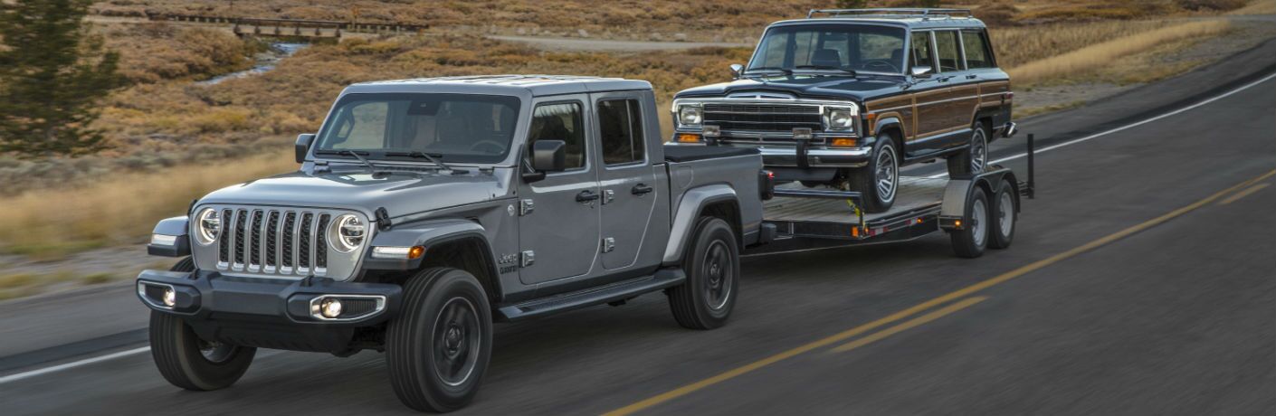 A photo of the 2020 Jeep Gladiator pulling a vehicle on a trailer on the road.