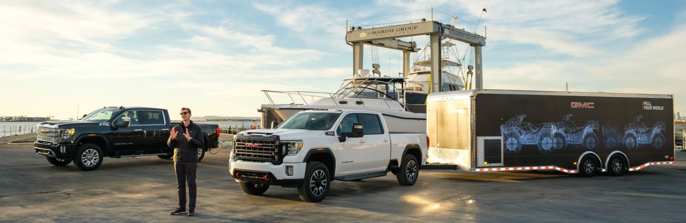 A photo of a man speaking in front of a pair of 2020 GMC Sierra 2500HD models at a ship yard.
