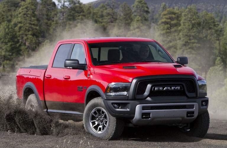 A red 2018 Ram 1500 kicking up dirt in an empty field in the woods