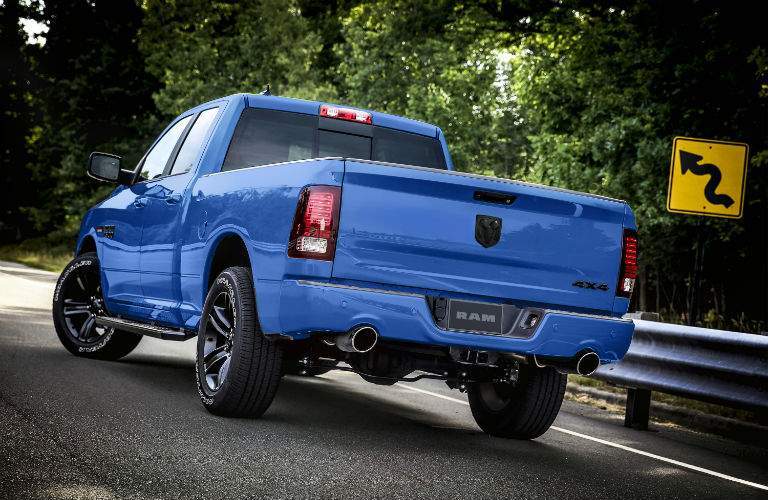 A blue 2018 Ram 1500 view from the rear of the truck parked on the side of a road