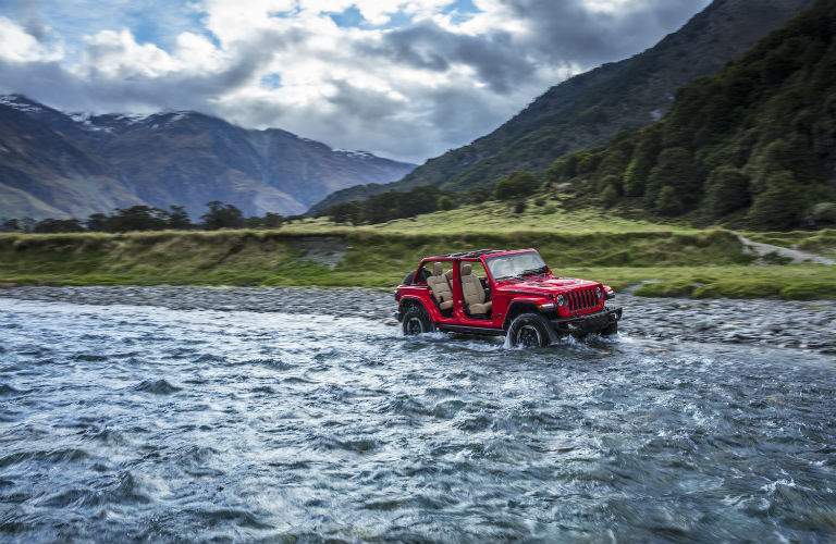 A photo of a 2018 Jeep Wrangler fording a river in the mountains