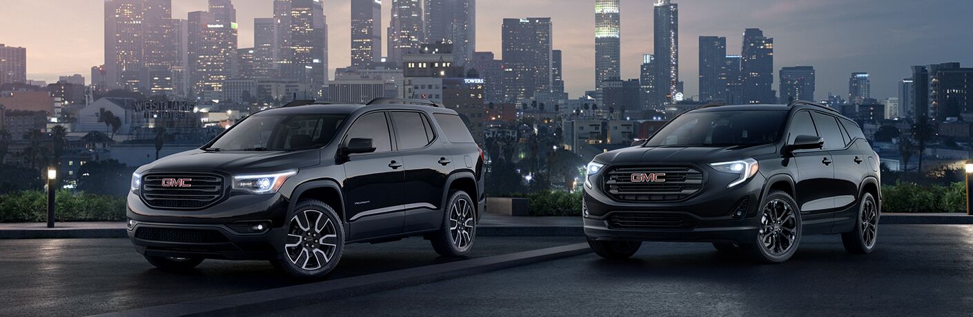 Exterior view of two black 2019 GMC Terrain models parked outside the city with skyscrapers in the background