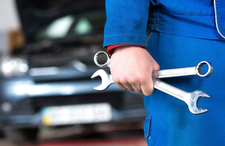 closeup of a mechanic hand holding wrenches with car in background