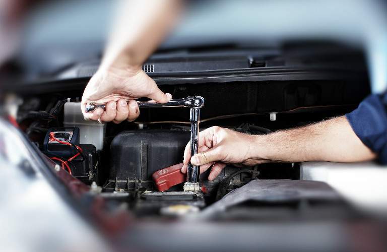 closeup of hands working underneath hood of car