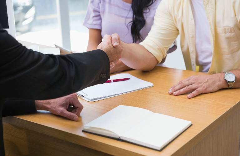salesperson shaking hands with a couple as paperwork is signed