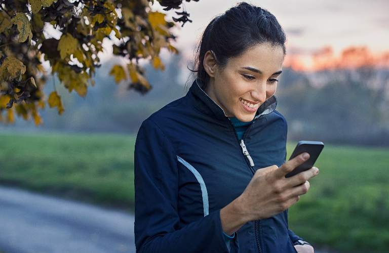 woman outside smiling while looking at phone