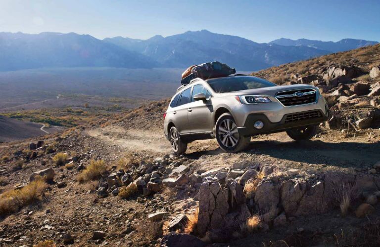 2018 Subaru Outback exterior front fascia and passenger side with cargo on roof and going up rocky dirt road