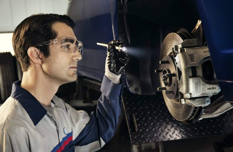 Ford Mechanic using flashlight to inspect vehicle brake system