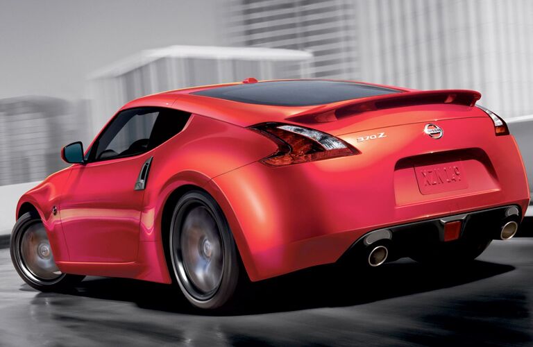 Sleek red 2019 Nissan 370Z coupe drives in a rainy city. Exterior rear/side angled view.