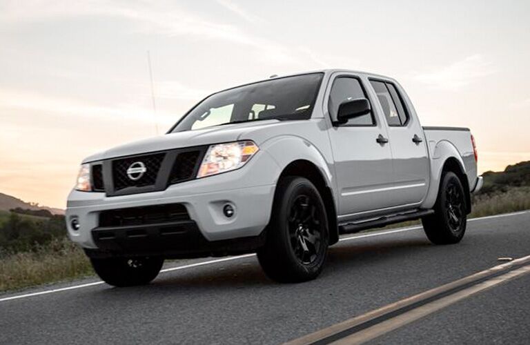 Low-angled view from the front of an off-white 2019 Nissan Frontier driving down a desert highway at dawn.
