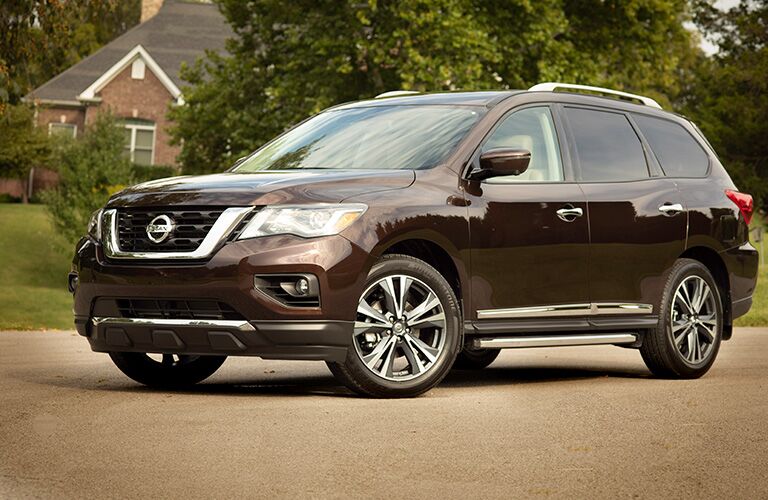 Brown 2019 Nissan Pathfinder exterior side/front angled view, parked on the street in front of a suburban brick homestead.