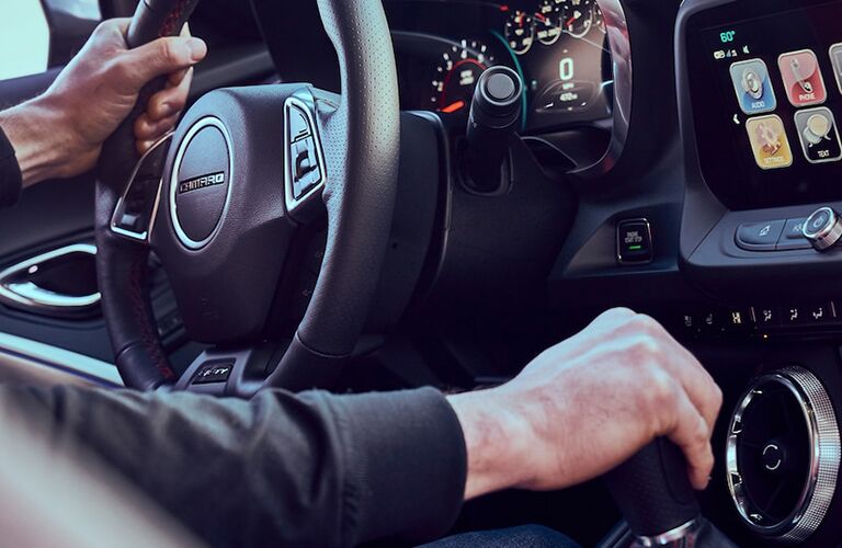 hands gripping the steering wheel and gear shift in a 2018 Chevy Camaro