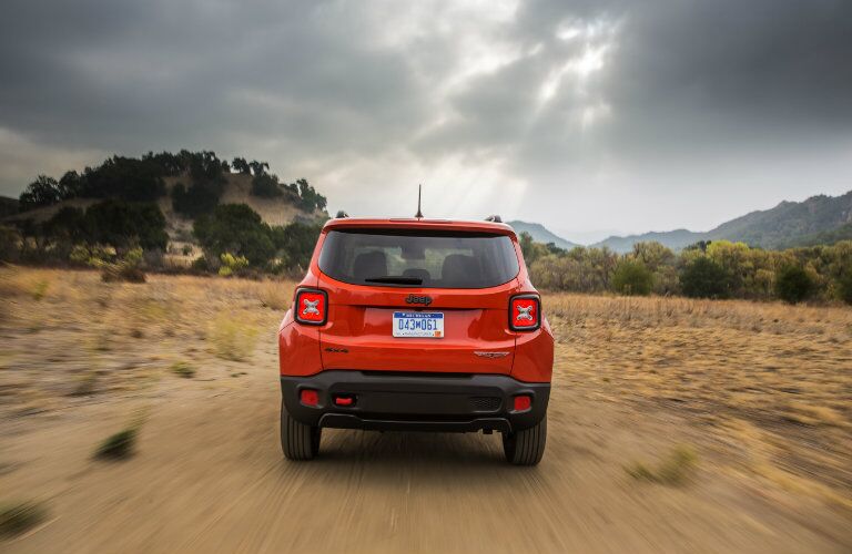 rear view of orange 2018 jeep renegade driving on dirt road