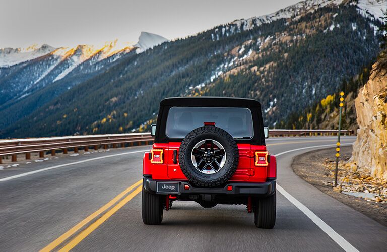 rear view of red 2018 jeep wrangler driving on highway with mountain ahead of it
