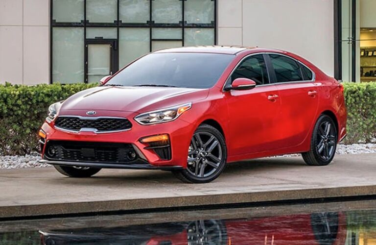 Exterior view of a red 2019 Kia Forte parked near a water feature outside an office building