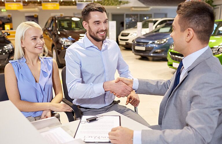 Couple Shaking Hands with Car Salesman in Dealership
