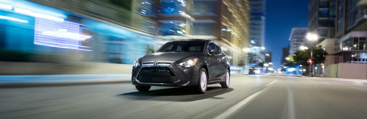 Gray 2018 Toyota Yaris iA driving down city street at night with lights illuminating path
