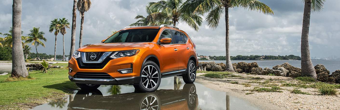 Orange 2018 Nissan Rogue parked in front of palm trees and water