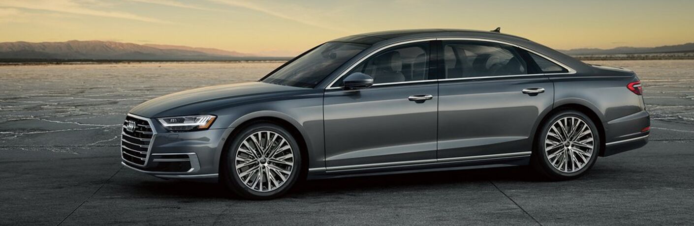 2019 Audi A8 exterior side shot with gray color paint job parked on a cracked plateau of earth and cement as the sun sets in the background