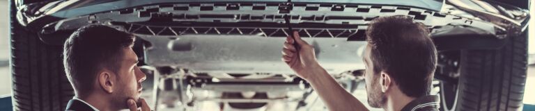 Two mechanics working on the underside of a vehicle