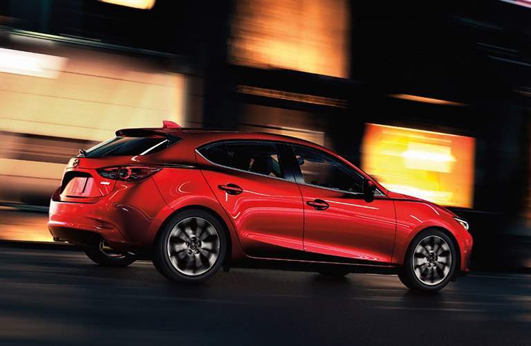red mazda3 five door driving fast in city