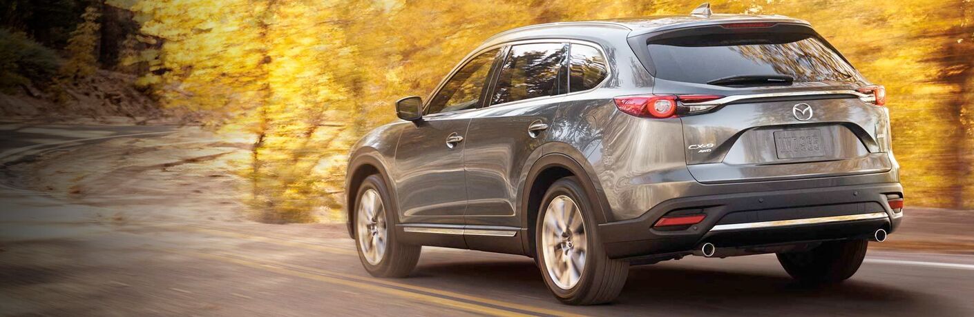 rear view of dark gray mazda cx-9 driving by fall trees