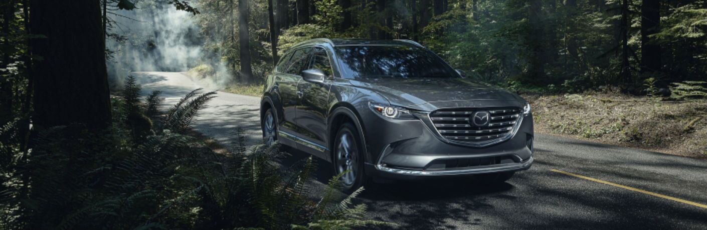 The front view of a gray 2021 Mazda CX-9 driving through the woods.