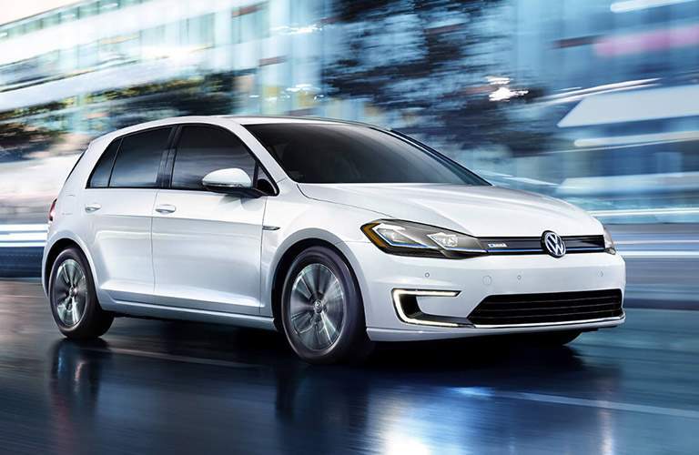 white volkswagen e-golf driving fast down street in city