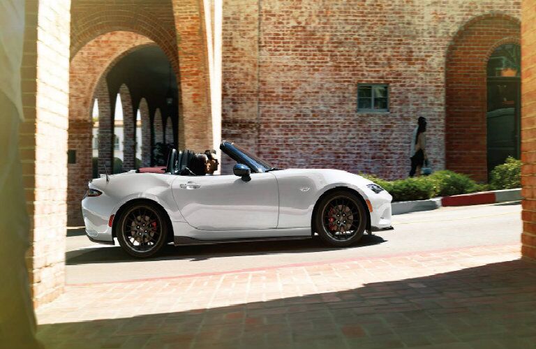2018 Mazda MX-5 Miata exterior shot white driving through street surrounded by brick roads, columns, and buildings