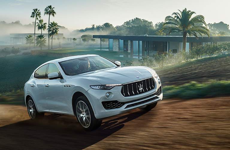 white 2017 Maserati Levante driving by a house with palm trees