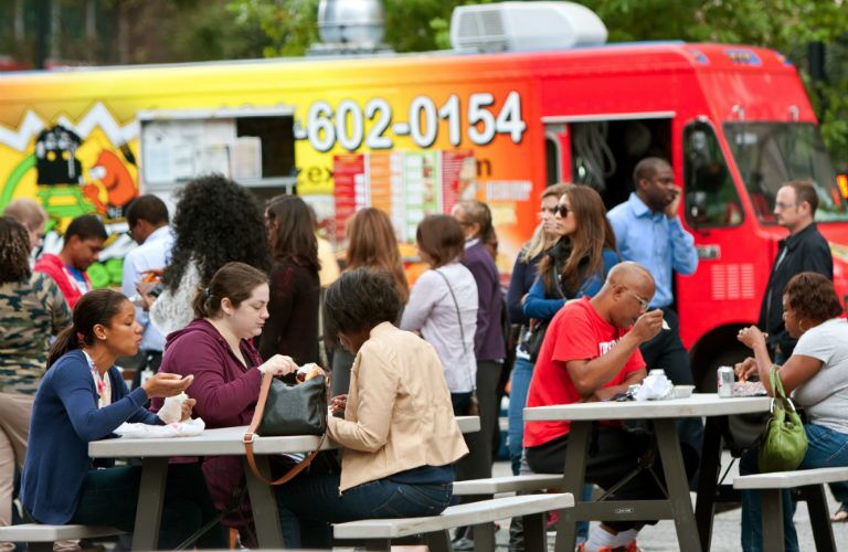 people eating on benches after getting food from a food truck