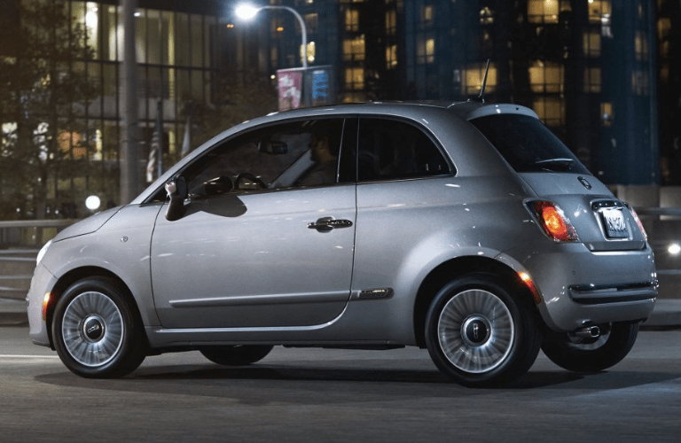Profile view of silver Fiat 500 driving on dark road