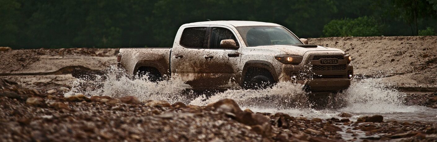 Profile view of white 2019 Toyota Tacoma TRD Pro driving through mud