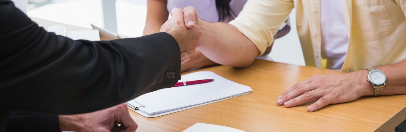 Two men shaking hands over a contract on a table at a dealership