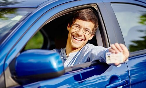young man sitting in a car holding his driver's license out the window