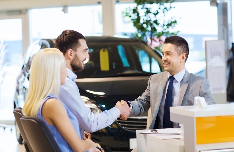 A salesman shakes the hand of a customer who sits beside a woman. Both seem satisfied with the transaction.
