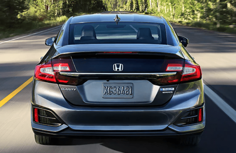 2021 Honda Clarity Plug-In Hybrid exterior rear shot with Modern Steel Metallic paint color driving on a forest highway