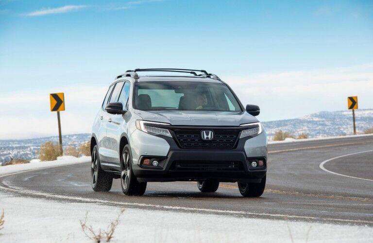2021 Honda Passport exterior shot with silver metallic paint color driving on a snowy mountain highway road