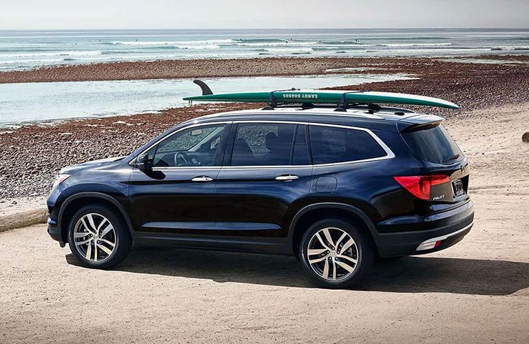 2018 Honda Pilot parked at a beach with a surfboard on top