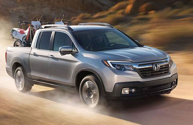 2018 Honda Ridgeline driving in a desert with dirt bikes in truck bed