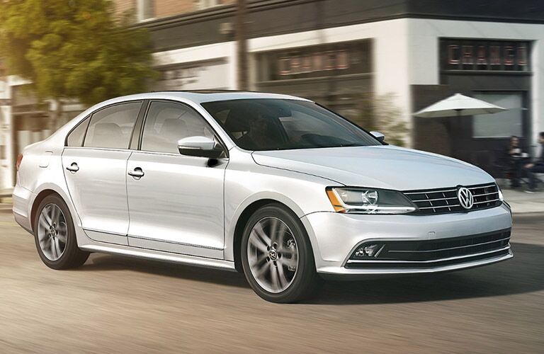 White 2018 Volkswagen Jetta driving down the road in front of a restaurant