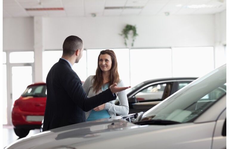 Car salesman talking to woman by car