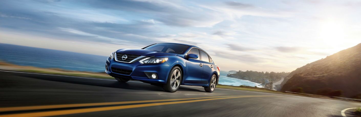 Blue Nissan Altima driving on an oceanside highway