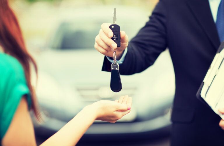 dealership worker passing car keys to woman driver