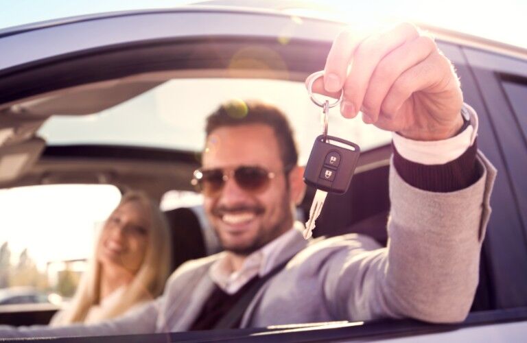 A man holding a car key out a car window