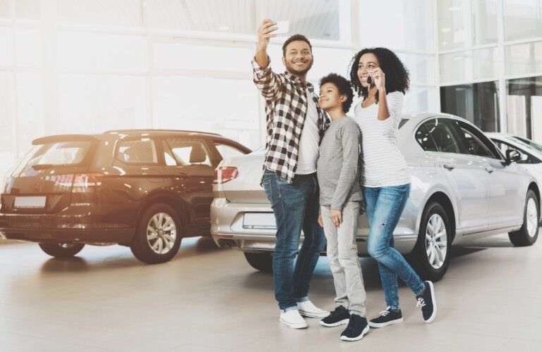An African American family holding car keys and taking picture with a smartphone in a car dealership